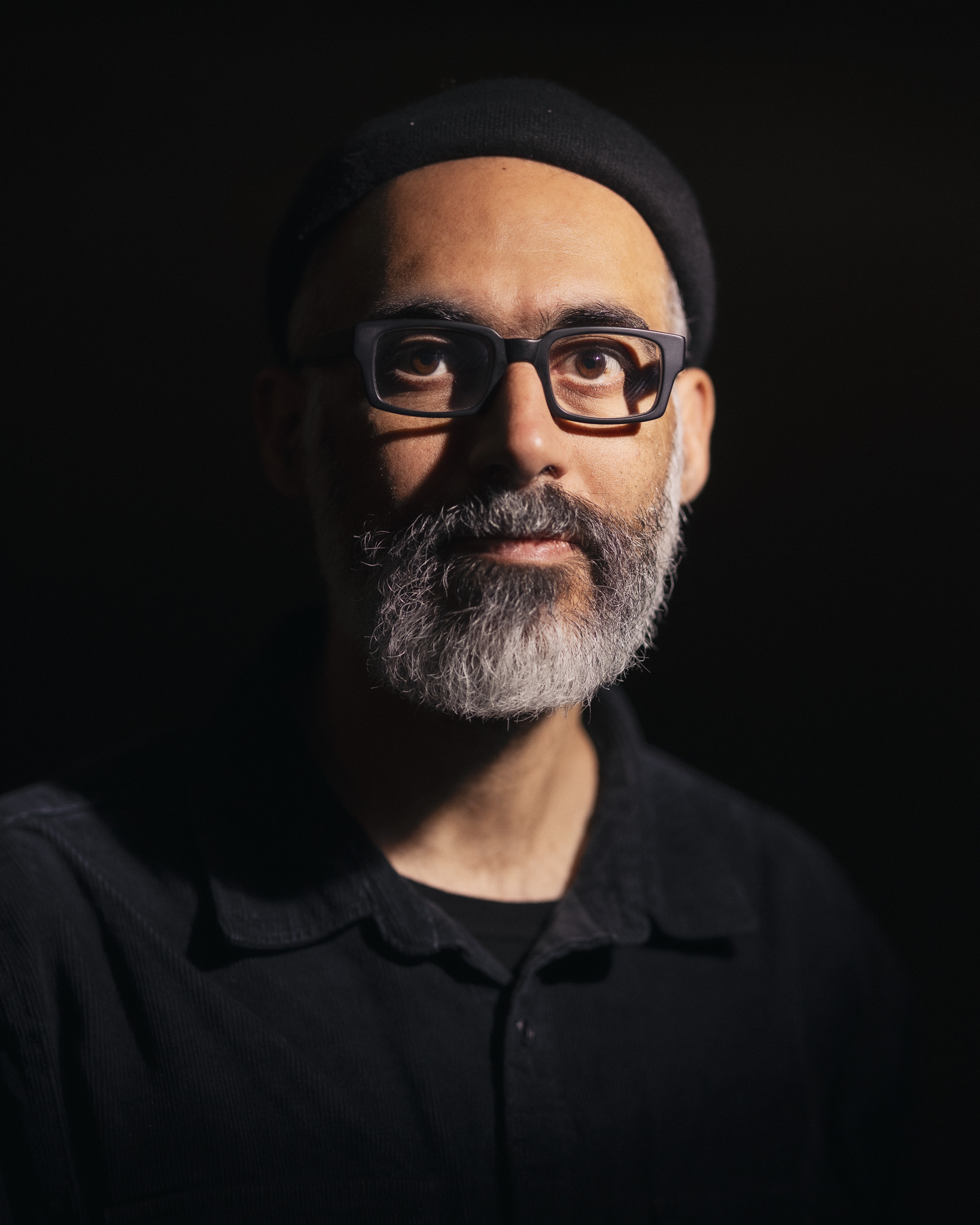 A portrait of Dirar Kalash. The background is black. A light shines on Dirar Kalash from the top right of the photo.